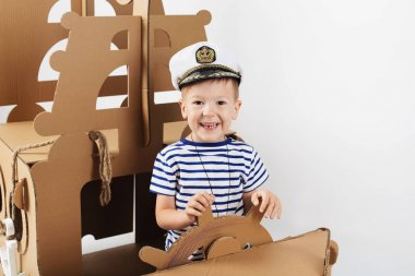 Beyaz zemin üzerine karton gemi ile oynarken küçük çocuk. Mutlu