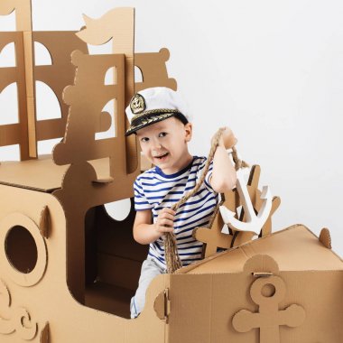 Beyaz zemin üzerine karton gemi ile oynarken küçük çocuk. Mutlu