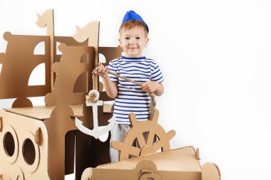 Beyaz zemin üzerine karton gemi ile oynarken küçük çocuk. Mutlu