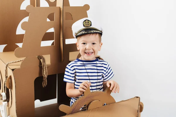 Beyaz zemin üzerine karton gemi ile oynarken küçük çocuk. Mutlu
