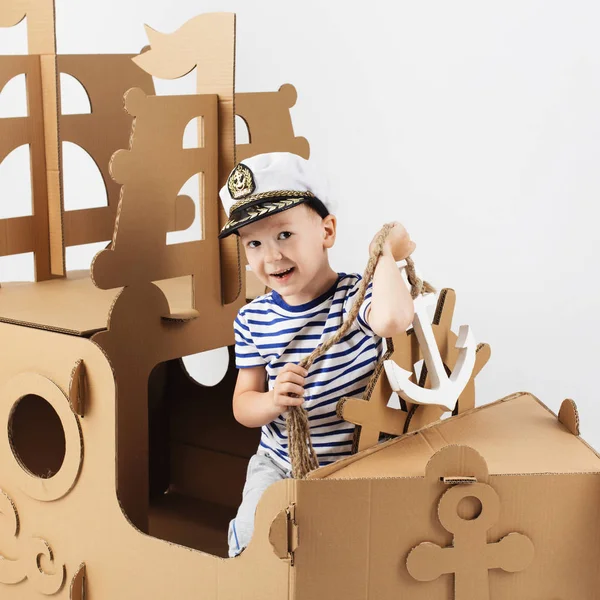 Beyaz zemin üzerine karton gemi ile oynarken küçük çocuk. Mutlu