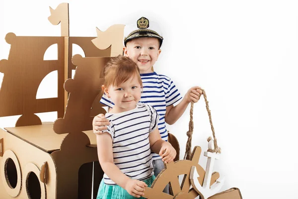 Маленькі діти грають з картонним кораблем на білому тлі. Щасливий — стокове фото