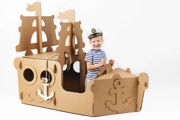Beyaz zemin üzerine karton gemi ile oynarken küçük çocuk. Mutlu — Stok fotoğraf