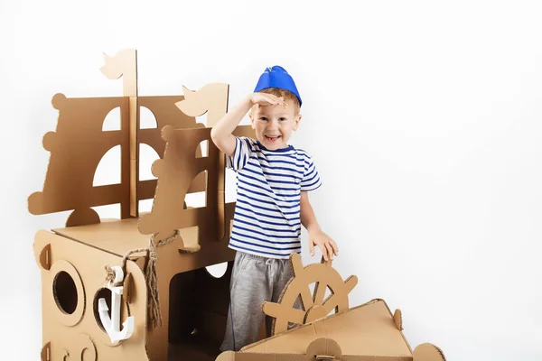 Little boy playing with cardboard ship on white background. Happ — Stock Photo, Image