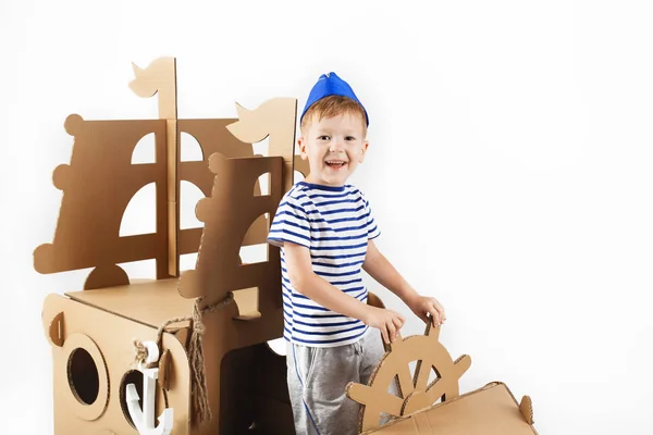 Little boy playing with cardboard ship on white background. Happ — Stock Photo, Image