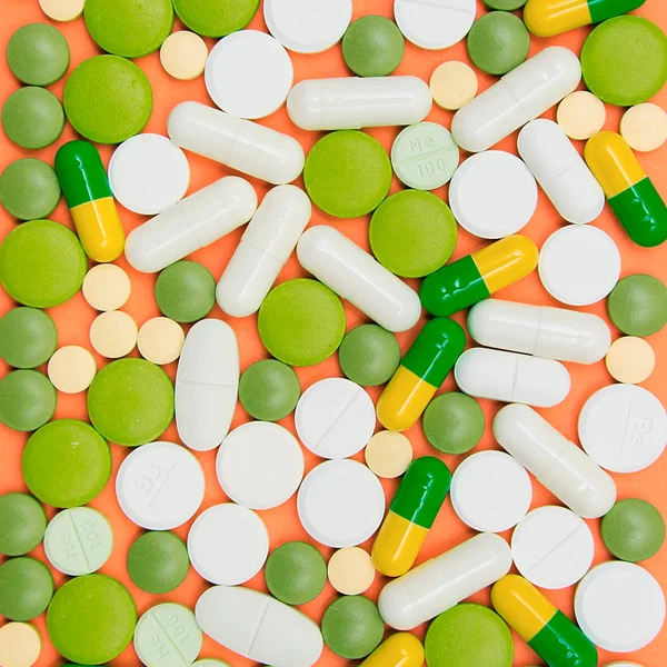 Капсулы с лекарствами и таблетки на оранжевом фоне — стоковое фото
