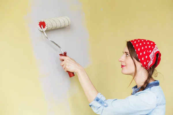 Beautiful girl in red Headband painting the wall with paint roll