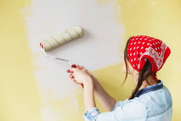 Bella ragazza in fascia rossa dipingere il muro con rullo di vernice — Foto Stock