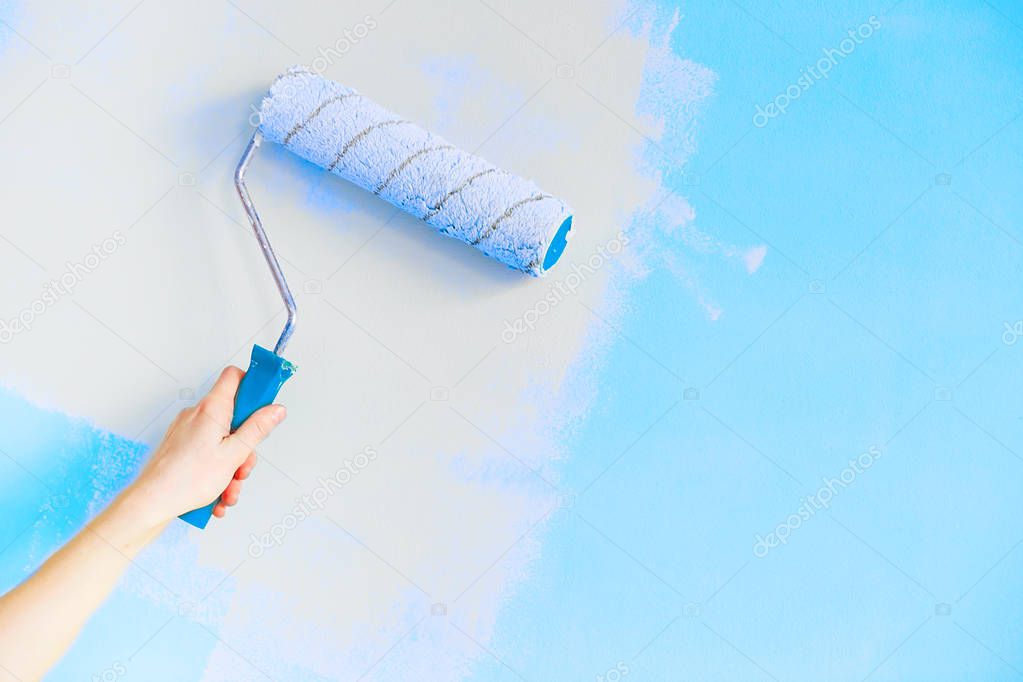 Female hand painting wall with paint roller. Close up of Decorat