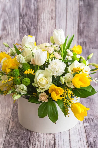 Bouquet of beautiful flowers with white peonies, roses, eustomas and yellow tulips, mimosa with green leaves in the papper gift box. Spring medley bouquet. Valentine's Day. Happy Mother's Day