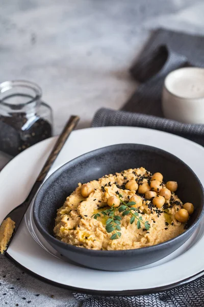 Chickpeas hummus in the black bowl decorated with sesame seeds and chickpeas greens. Vegan recipes, plant-based dishes. Green living concept. Organic food. Vegetarian cuisine.