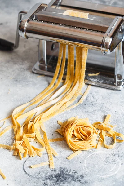 Metal pasta maker with dough. Fettuccine coming out of a manual pasta machine. Making noodles with pasta machine. Pasta maker with dough on light background.