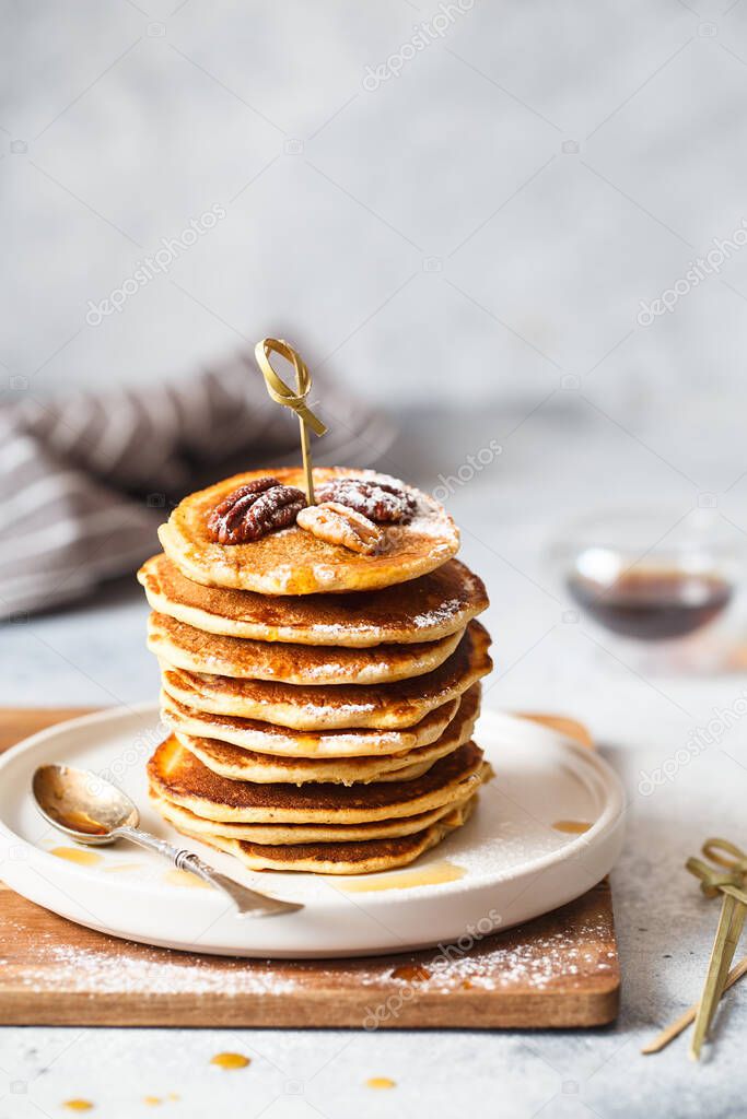 Homemade classic american pancakes with pecans and maple syrup, served with fingerfood sticks. Stack of small pancakes with bamboo brochettes on light grey background. American cuisine. Healthy breakfast