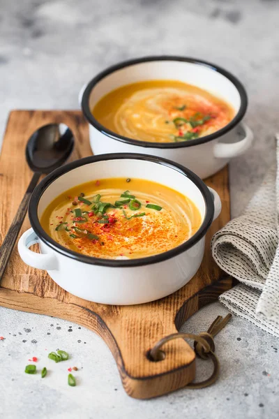 Pumpkin cream soup. Roasted pumpkin and carrot puree soup with turmeric, cream, paprica, chives and pumpkin seeds on grey background. Vegetarian cousine. Vegan recipe. Green living. Organic food.