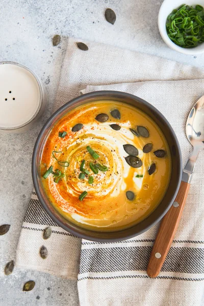 Pumpkin cream soup. Roasted pumpkin and carrot puree soup with turmeric, cream, paprica, chives and pumpkin seeds on grey background. Vegetarian cousine. Vegan recipe. Green living. Organic food.