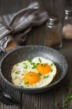 Kahvaltı için yeşil soğanlı sahanda yumurta. Koyu ahşap arka planda küçük bir tavada iki kızarmış yumurta. Kırsal biçim. 