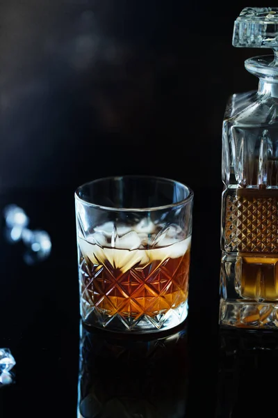 Glass of whiskey or bourbon with ice on black stone table. Glass of whiskey with ice and a square decanter. Glass of scotch whiskey and ice.