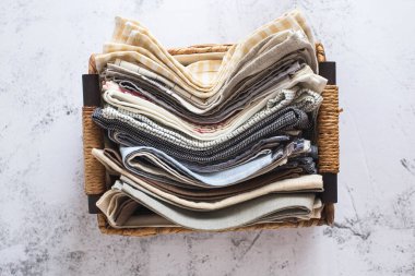 Mutfak tekstili. Farklı renk ve dokularda kumaş yığını, yakın plan. Beyaz arka planda mutfak havluları. Hasır sepetin içinde birçok kumaş mutfak peçetesi var. Yemek fotoğrafı için dekor