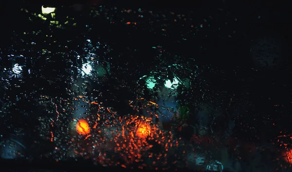 Estrada da cidade vista através de gotas de chuva no pára-brisas do carro à noite — Fotografia de Stock