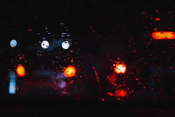 夜幕降临时从雨点中看到的城市道路在汽车挡风玻璃上 — 图库照片