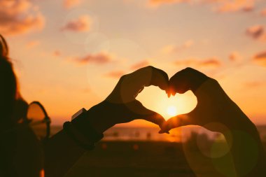 Girls hands in heart shape with sun light and colorful sky on th