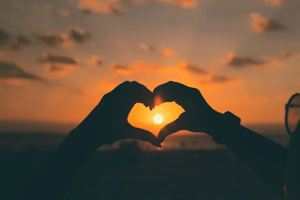 Las niñas manos en forma de corazón con luz solar y cielo colorido en th —  Fotos de Stock