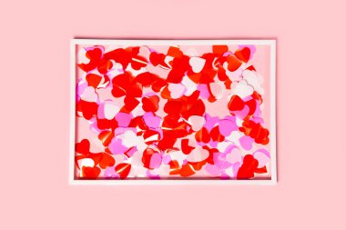 Colorful confetti in a heart shape with white frame on pink back