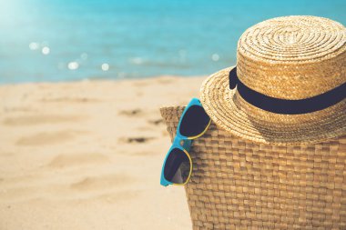 Saman çanta, hasır şapka ve gün batımında deniz plajı ile güneş gözlüğü l