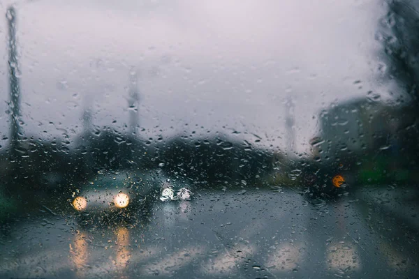 Şehir yolu, arabanın ön camına düşen yağmur damlalarının arasından görülüyor. Su damlalarına odaklan.