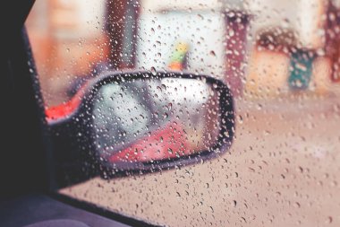 Dikiz aynası yağmur görülen araba camına düşüyor. Bazı su damla üzerinde odaklanmıştır.