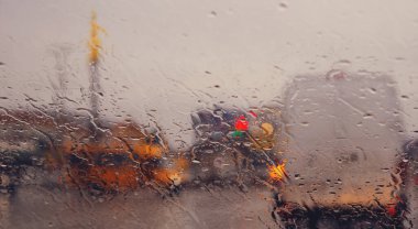 Şehir yolu, arabanın ön camına düşen yağmur damlalarının arasından görülüyor. Su damlalarına odaklan.
