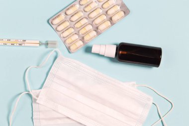 Tıbbi maskeler, el dezenfektanı, haplar ve mavi arka planda termometre. Coronavirus koruma kavramı