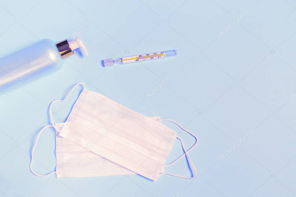 Medical masks, hand sanitizer gel and thermometer on pastel blue background. Coronavirus protection concept