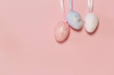 Renkli pastel arka planının yanında asılı duran dekoratif paskalya yumurtaları. Mevsimlik kartlar, bloglar ve web tasarımı için tatil arkaplanı. Asgari biçim