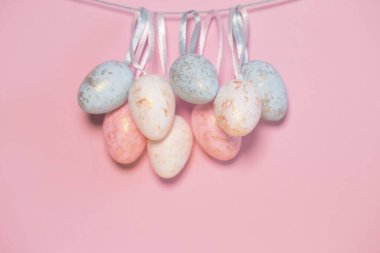 Renkli pastel arka planının yanında asılı duran dekoratif paskalya yumurtaları. Mevsimlik kartlar, bloglar ve web tasarımı için tatil arkaplanı. Asgari biçim