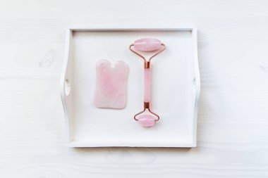 Gül kuvarstan yapılmış yüz masajı seti. Tahta arka planda yüz silindiri ve gua sha masaj aleti.
