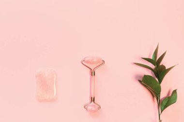 Yüz masajı seti. Yüz silindiri ve gua sha masaj aleti pastel pembe arka planda doğal taşlardan yapılmış. Cilt bakımı kavramı