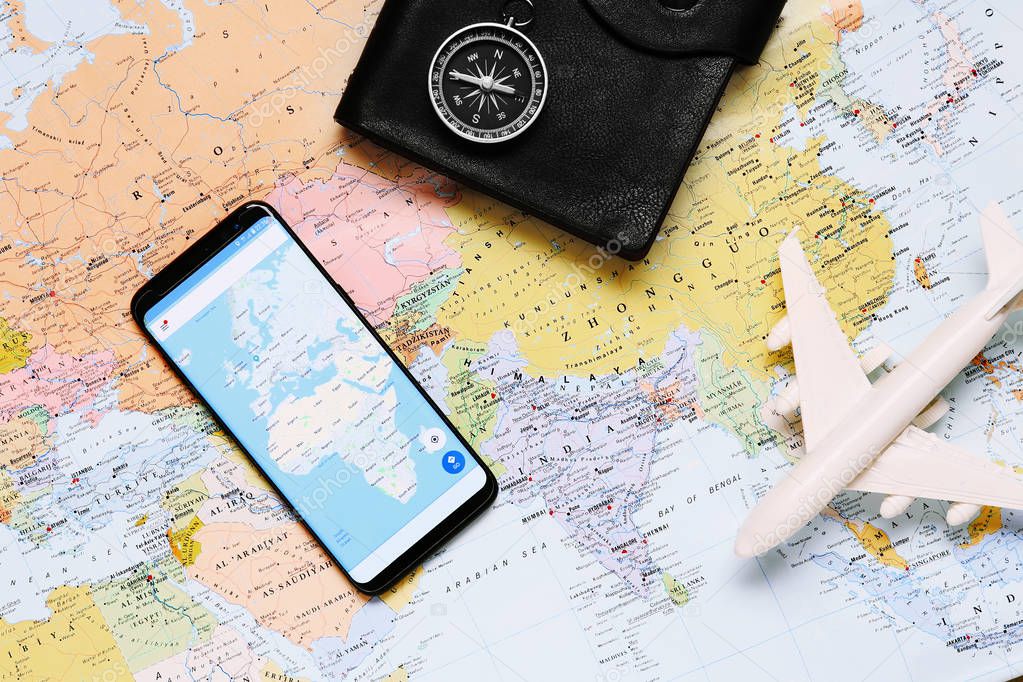 Compass, toy airplane and mobile phone on world map background 