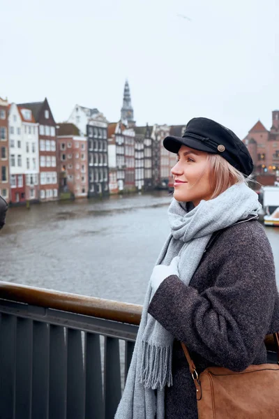 Jonge vrouw staat op de brug en kijkt naar het kanaal van Amsterdam, Nederland. — Stockfoto