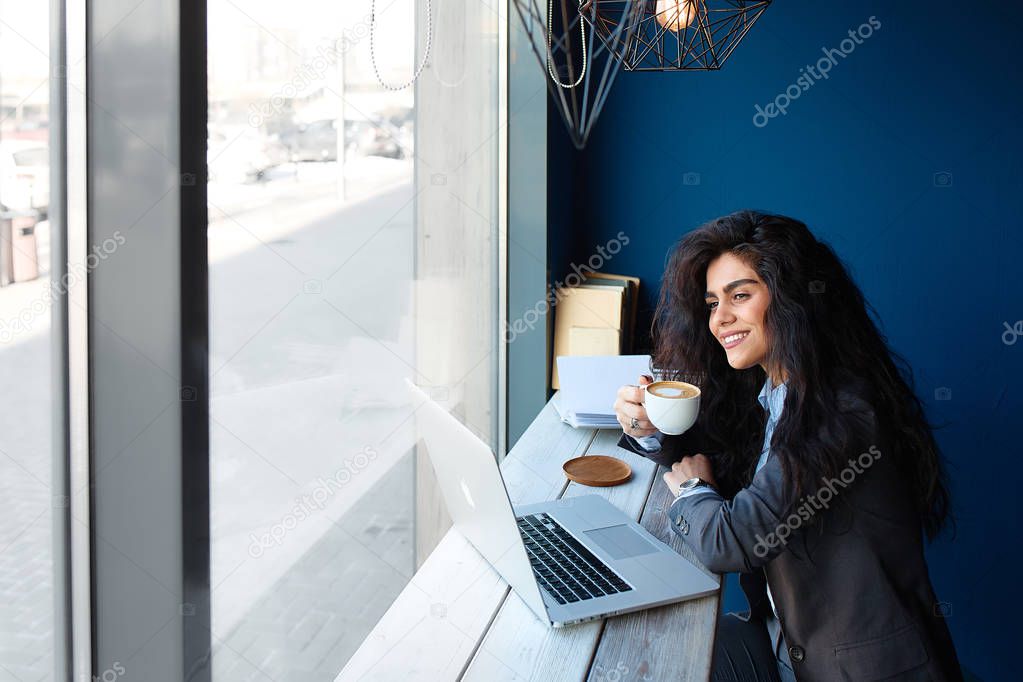 Beautiful brunette sitting in coffee shop and working on computer.