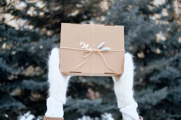 Женщина с подарком или подарочной коробкой на улице. Руки в вязаных варежках. Ношение стильной теплой одежды — стоковое фото