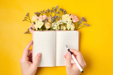 Sarı arka planda çiçekler olan pembe not defteri. Bahar havası