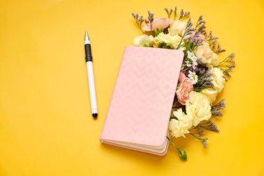 Sarı arka planda çiçekler olan pembe not defteri. Bahar havası