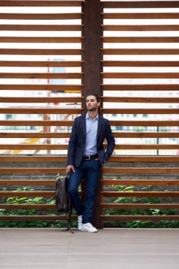 Sırt çantalı, klasik takım elbiseli çekici sakallı genç adam.