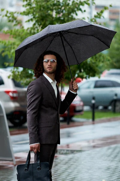 Man holds open umbrella. handAttractive bearded young man in classic suit with bag