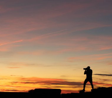 Güneş batarken binanın tepesinde duran bir adam kamerayla fotoğraf çekiyor.