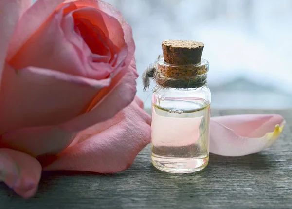 Rose essential oil in a glass bottle with pink rose flower on old wooden table.Rose oil for spa and bodycare.