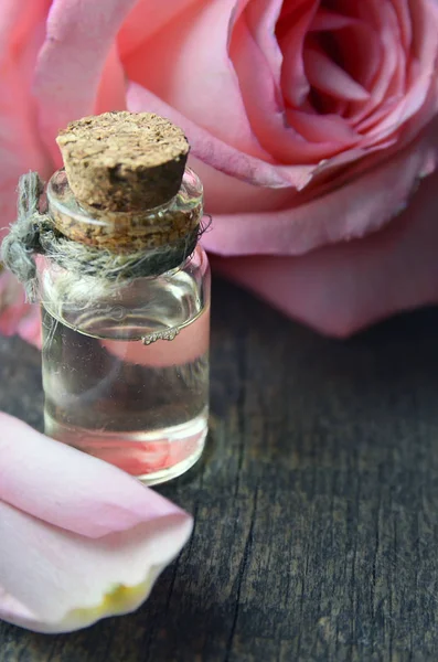 Rose essential oil in a glass bottle with pink rose flower on old wooden table.Rose oil for spa and bodycare.