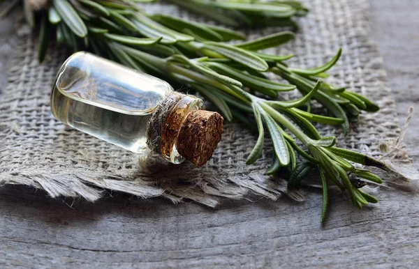 Rosemary essential oil in a glass bottle with fresh green rosemary herb on old wooden table.