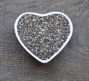 Beyaz kalp içinde Chia tohum eski ahşap arka plan üzerinde kase şeklinde. Ada çayı hispanica tohumları. Sağlıklı gıda veya superfood kavramı.
